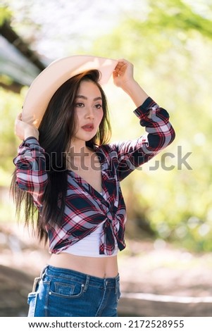 Beautiful cowgirl style model posing on farmland. Young adult Asian woman fashion in natural environment. 