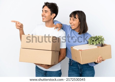Young couple making a move while picking up a box full of things isolated on white background pointing to the side to present a product