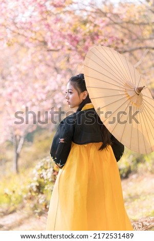 Korean girl wearing a hanbok wearing yellow umbrella. Beautiful Female wearing traditional Korean hanbok with cherry blossom in spring, seoul, Korea. Royalty-Free Stock Photo #2172531489
