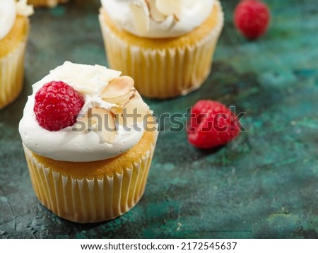 Cupcakes with white cream, raspberries and almonds on a dark green background. Children and youth culture, fast food, light summer dessert, birthday, holiday treat.