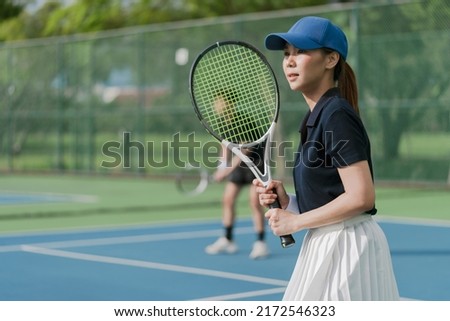 Asian young couple playing tennis on a tennis outdoor court on a bright sunny day. Sport activity, tennis training and competition concept