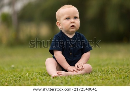 beautiful baby sitting on the green grass in a blue dress