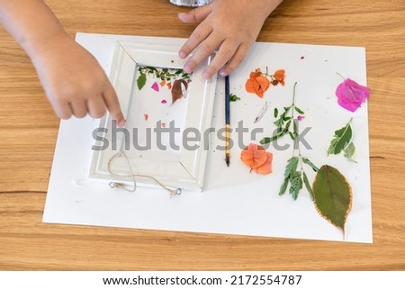 Faceless kid arranging pressed flowers onto a picture frame.