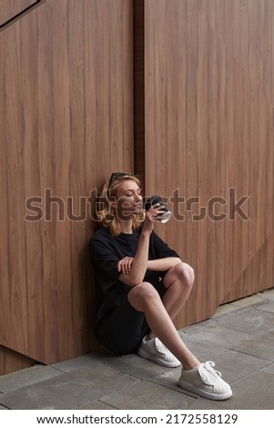 Awesome girl with blonde hair holding a cup of coffee. Woman on the wooden background. Good morning. Sport wearing.