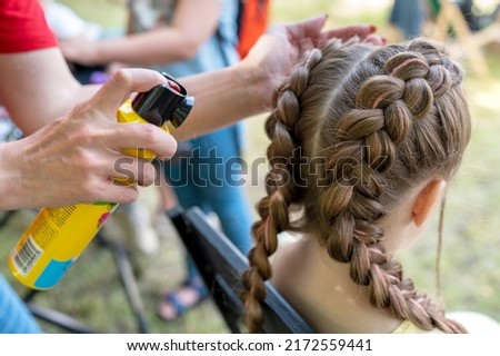 Braids hairstyle with woven pink threads. Hair stylist makes a hairstyle and fixes it with hairspray. Pigtails on the girl's head. Royalty-Free Stock Photo #2172559441