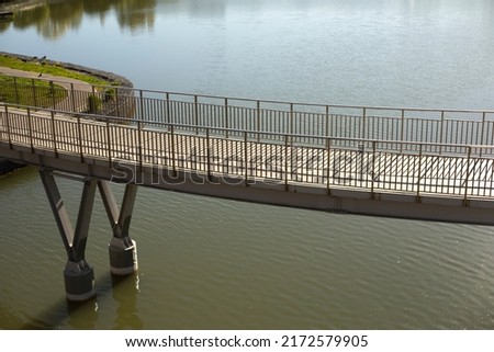 Pedestrian bridge on water. Bridge with railings. Details of park in city. Embankment on lake. Royalty-Free Stock Photo #2172579905