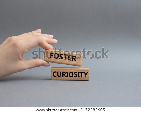 Foster curiosity symbol. Concept word Foster curiosity on wooden blocks. Beautiful grey background. Businessman hand. Business and Foster curiosity concept. Copy space Royalty-Free Stock Photo #2172585605