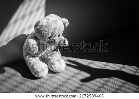 Damaged and dirty teddy bear under casted shadow, representing a child in a bad or scary situation: nightmare, child abuse, domestic violence, kidnapping or parental neglect Royalty-Free Stock Photo #2172589463