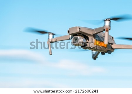A modern quadrocopter soars in the air against a blue sky, a drone