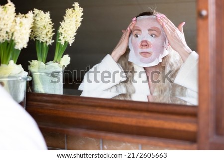 a middle-aged woman is busy with morning hygiene, she makes the face mask 