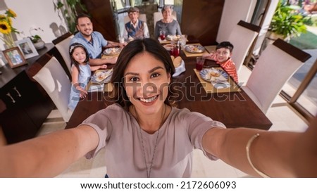 Beautiful Latin woman makes a selfie with her cell phone to keep the memory of grandparents, parents and grandchildren together at the table. Latin family.