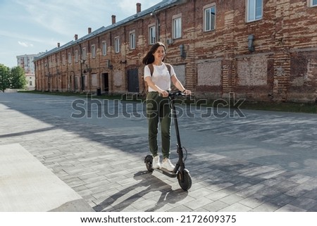 Woman in white t shirt and sneakers rides an electric scooter Royalty-Free Stock Photo #2172609375