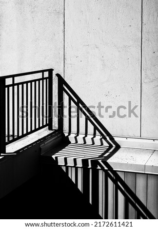 Black and White View of a Black Metal Railing with Shadows against a White Building Wall.