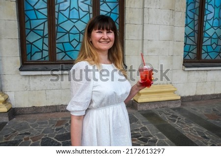 Smiling woman in white dress holding fresh lemonade with ice. Summer holiday