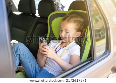 Beautiful children watch a movie on a tablet while sitting in a car. Little girl in a car seat enjoying a ride
