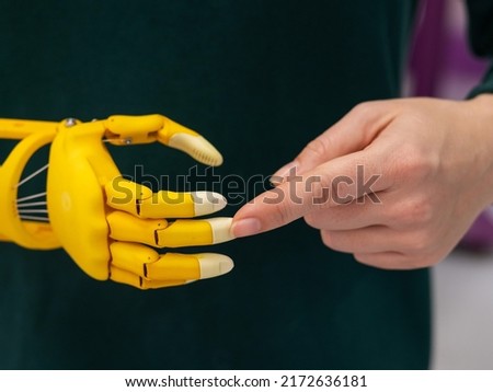 A woman demonstrates a plastic children's prosthetic hand printed on a 3D printer.  Royalty-Free Stock Photo #2172636181