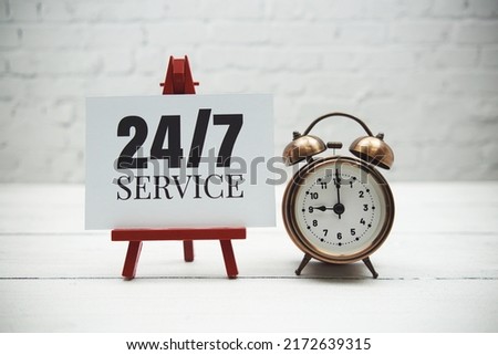 24 Hour  text and alarm clock on white brick wall and wooden background Royalty-Free Stock Photo #2172639315