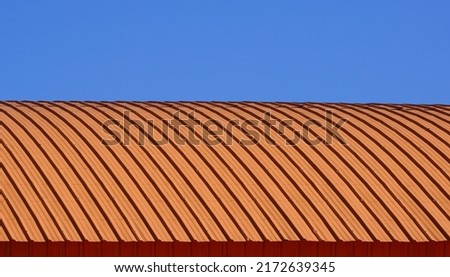 Curve line pattern of orange corrugated steel curved roof against blue clear sky background Royalty-Free Stock Photo #2172639345