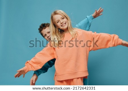 two cute children of school age in multi-colored sweaters stand on a blue background, a boy and a girl stand with their hands apart, depicting airplanes. The theme of friendship between children Royalty-Free Stock Photo #2172642331