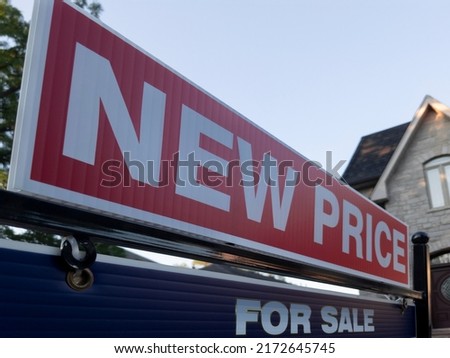 Sign for sale new price by detached house in residential area. Real estate market volatility,  bubble, crash, hot and cooling housing market, overpriced property, buyer activity concept.  