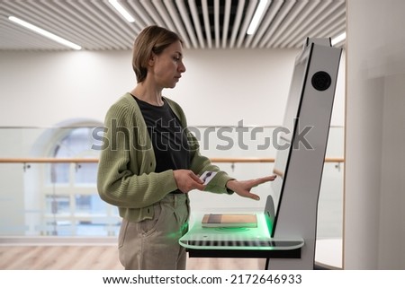 Middle-aged woman using self-service terminal in digital library space, registering book, searching and selecting literature or browsing catalogue. Innovative technologies in libraries