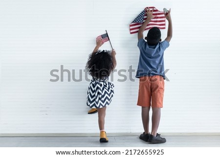 African American kid boy and girl hanging American flag on white wall, independence day, 4th July concept.