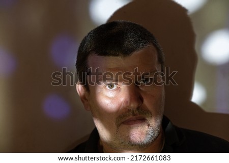 A portrait of a quiet man against the wall. A beam of light illuminates his right eye. A middle-aged male with short graying brown hair. The man looks confidently into the camera. Selective focus.