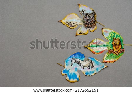 Fallen tree leaves with animals drawn on them. Funny drawings of a bear cub, an owl and a horse. Gouache, acrylic. Gray background. Modern art. View from above.