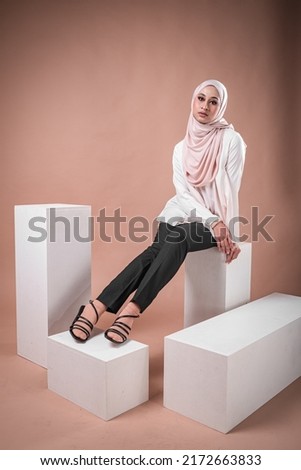 Portrait of a beautiful female model wearing hijab, a lifestyle apparel for Muslim women isolated on brown background. Idul Fitri and hijab fashion concept.