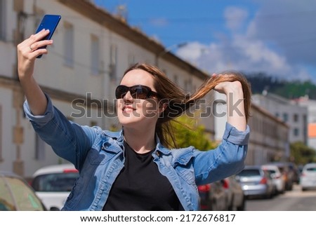 smiling woman taking a selfie on the street with her smartphone