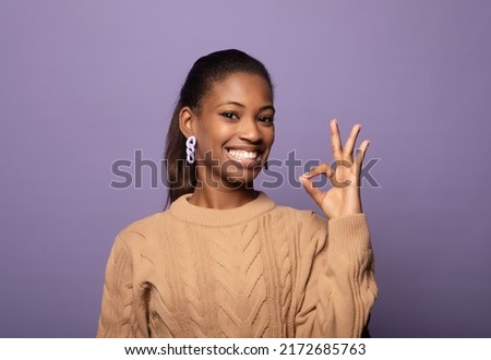 Content afro american woman in beige sweater smiling on camera and gesturing ok sign isolated over purple background