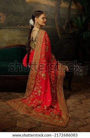Charming young woman is sitting on the sofa. Traditional Indian wedding sari and jewelry.