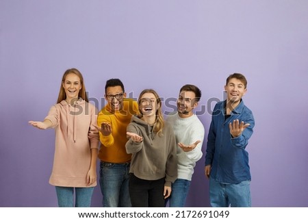 Diverse group of happy cheerful young multiethnic people standing together, looking at the camera, smiling, extending their hands and doing an inviting gesture, telling you 'Come here and join us'