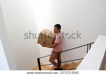 Latin adult man carries a cardboard box on the stairs of his house during a move opens house that he bought in real estate very happy for the change
