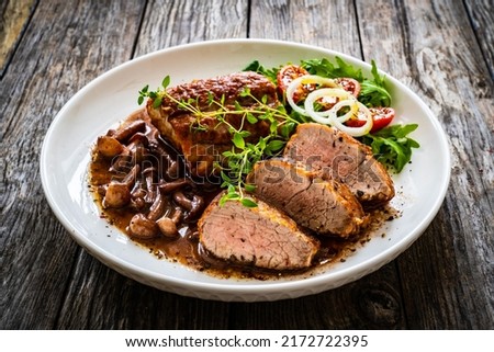 Roasted pork loin with shimeji mushrooms in sauce, fresh thyme, greens and cherry tomatoes on wooden table  Royalty-Free Stock Photo #2172722395