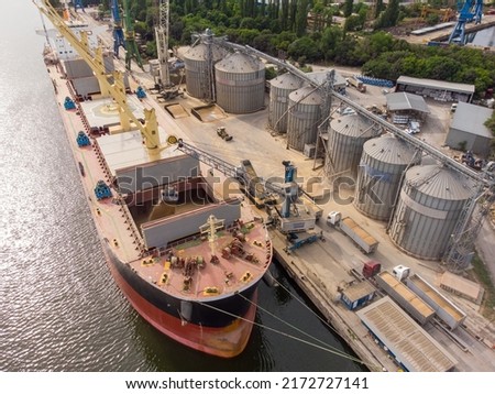 Loading grain into holds of sea cargo vessel in seaport from silos of grain storage. Bunkering of dry cargo ship with grain. Aerial top view Royalty-Free Stock Photo #2172727141