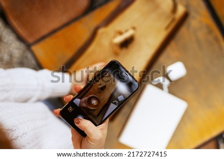 Woman hands taking a picture of a coffee cup with smart phone and laptop at a coffee shop. 