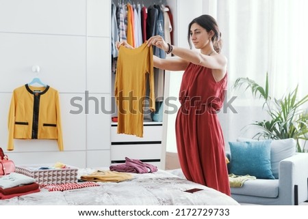 Elegant woman in her bedroom, she is decluttering her wardrobe and choosing clothes Royalty-Free Stock Photo #2172729733