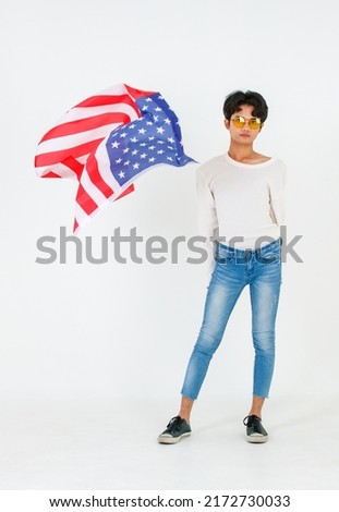 Portrait studio shot of Asian young LGBT gay bisexual homosexual male fashionable model in casual outfit and fashion sunglasses standing holding waving flying USA national flag on white background.
