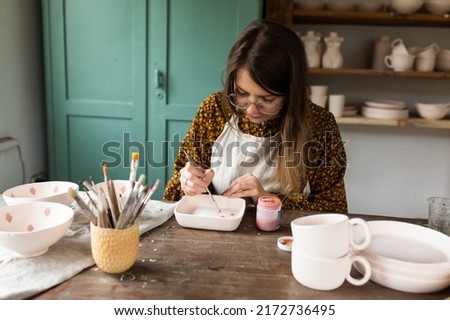 Young talented woman painter at work. Woman artist in glasses in workshop	
