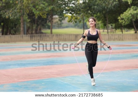 Athletic young asian woman in sportswear standing and skipping rope outdoor for morning exercise. Active and healthy girl workout on biceps exercise with tree background. Sport and lifestyle concept Royalty-Free Stock Photo #2172738685