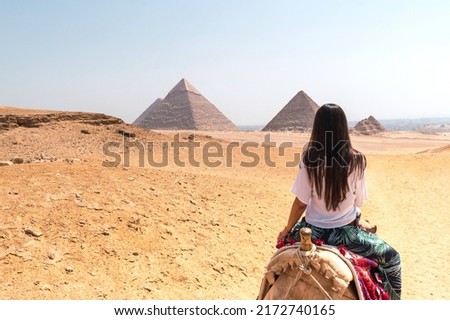 Woman with long dark hair mounted on a dromedary on her back looking at the pyramids of Egypt Royalty-Free Stock Photo #2172740165
