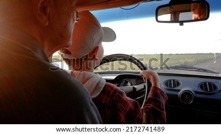Grandfather teaches grandson to drive. The child sits on his hands and turns the steering wheel of the car Royalty-Free Stock Photo #2172741489