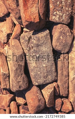 Stone wall of old stones of different colors with white spots. Textured vertical background of wall of stones.