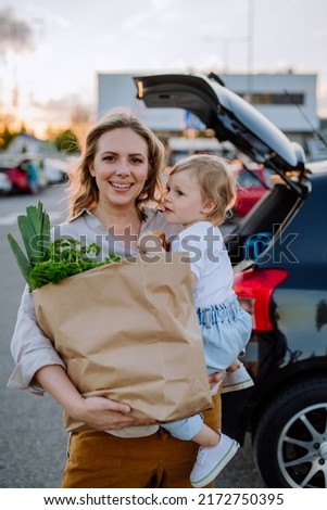 Young mother with little daughter after shopping holding zero waste shopping bags with grocery near car. Royalty-Free Stock Photo #2172750395