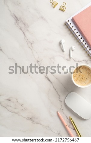 Business concept. Top view vertical photo of workstation pink organizers pens gold binder clips computer mouse wireless earbuds and cup of hot drinking on white marble background