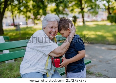 Grandchild surprised her grandmother with a birthday present in the park. Lifestyle, family concept Royalty-Free Stock Photo #2172757275