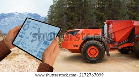Man controls autonomous mining truck using digital tablet. Remotely operated industrial vehicle concept. Royalty-Free Stock Photo #2172767099