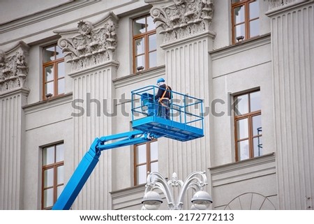 Construction worker in lift bucket of crane restore and repair historic facade of building. Man in cradle, restoring plaster decoration on facade. Workers painting building, renovating and repair work Royalty-Free Stock Photo #2172772113