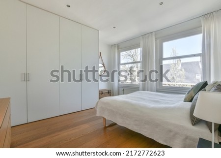 Home interior design of bedroom with bed and wooden wardrobe placed in corner near window in modern apartment Royalty-Free Stock Photo #2172772623